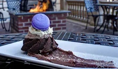 Spiral dark chocolate dessert with cream and macaron on an outdoor table.