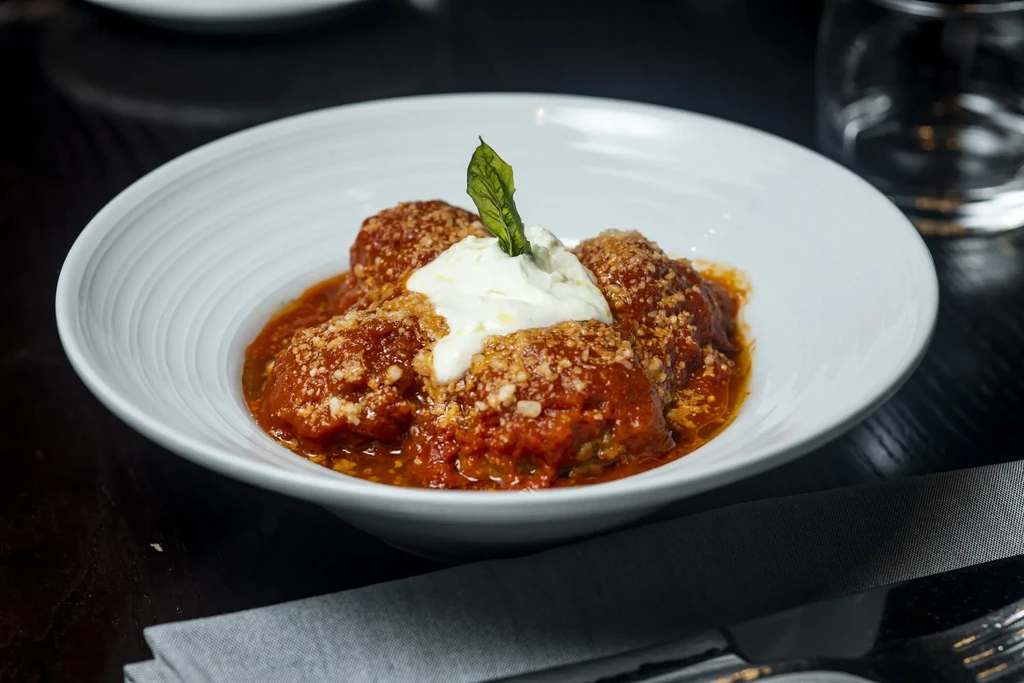 Meatballs in tomato sauce with cheeses and basil in a white bowl.