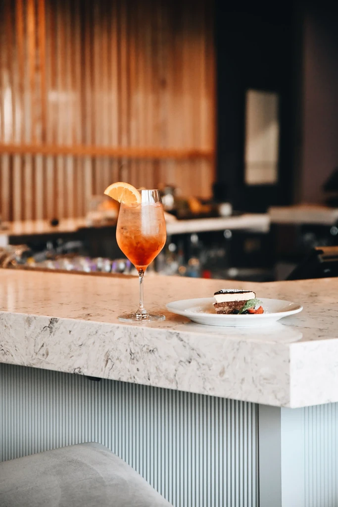 Stemmed orange cocktail and dessert with strawberries on marble countertop.