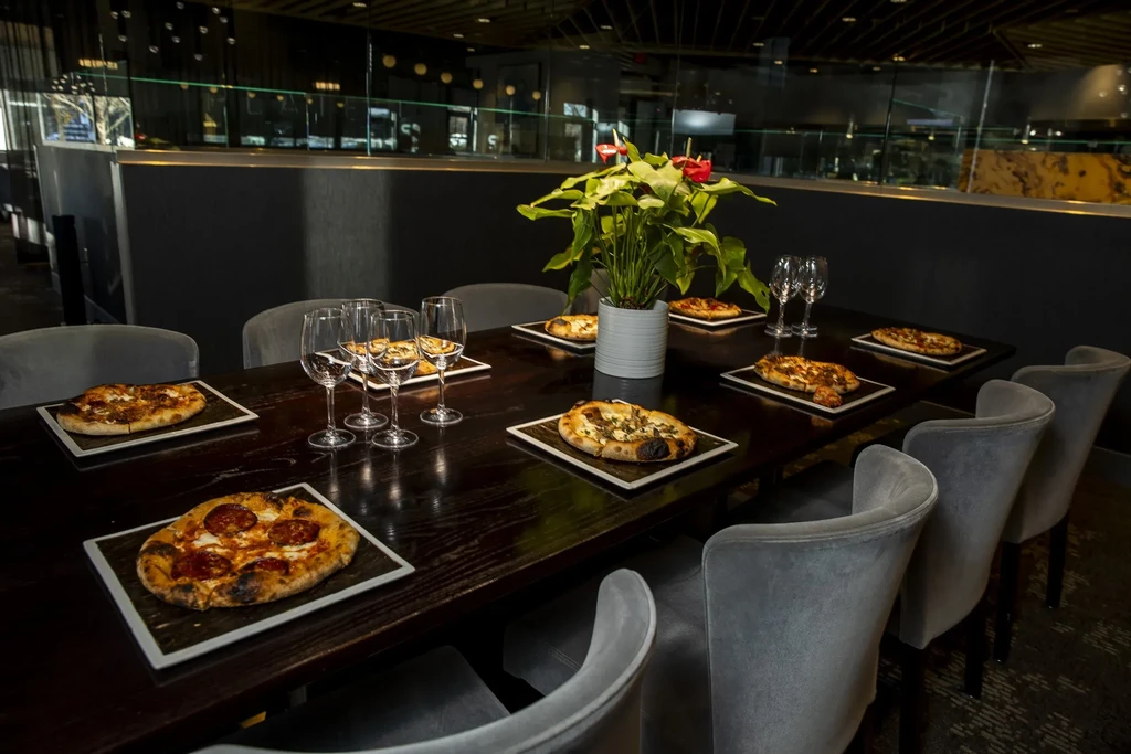 Dark wooden table with individual pizzas, wine glasses, and anthurium.