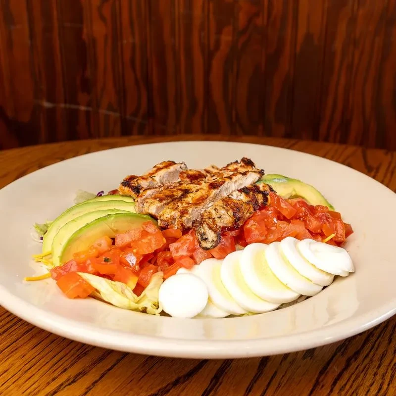 Grilled chicken salad with fanned avocado, tomatoes, and egg slices.