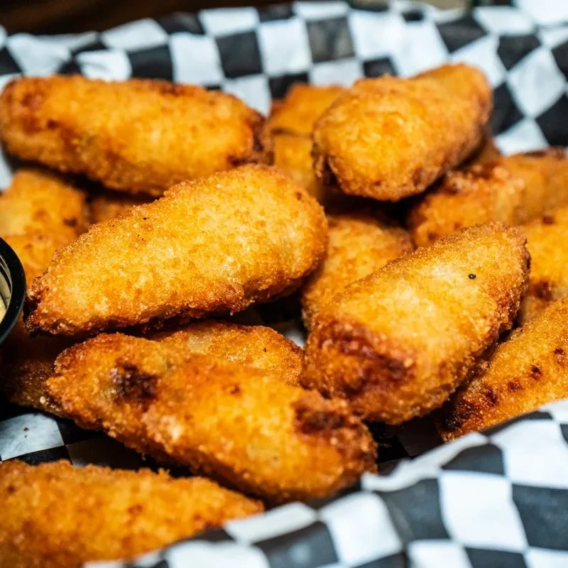 Golden-brown fried appetizers in a checkered basket, with a dipping sauce.