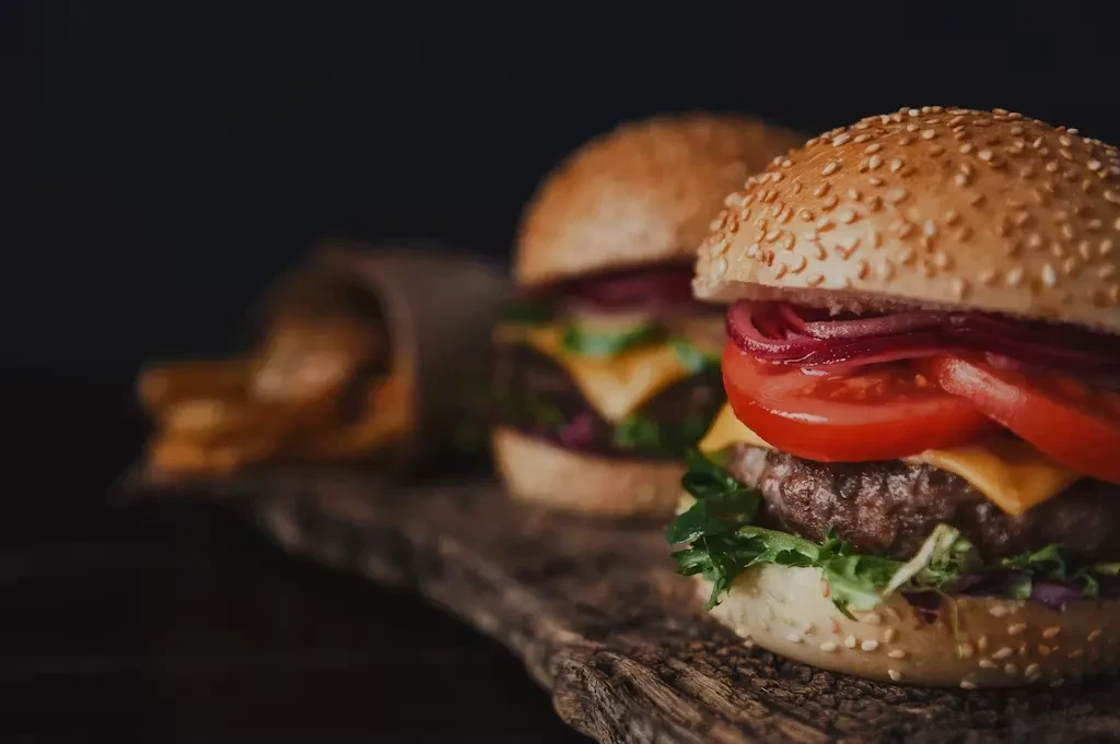 Close-up of two gourmet burgers and fries on a rustic wooden board.