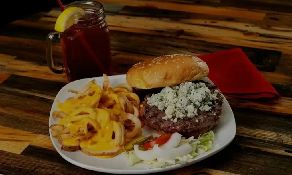Blue cheese burger, curly cheese fries, and a drink on a wooden table.