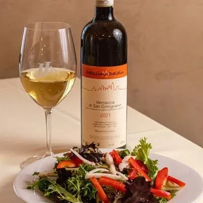 White wine bottle, glass, and fresh salad on a white table.