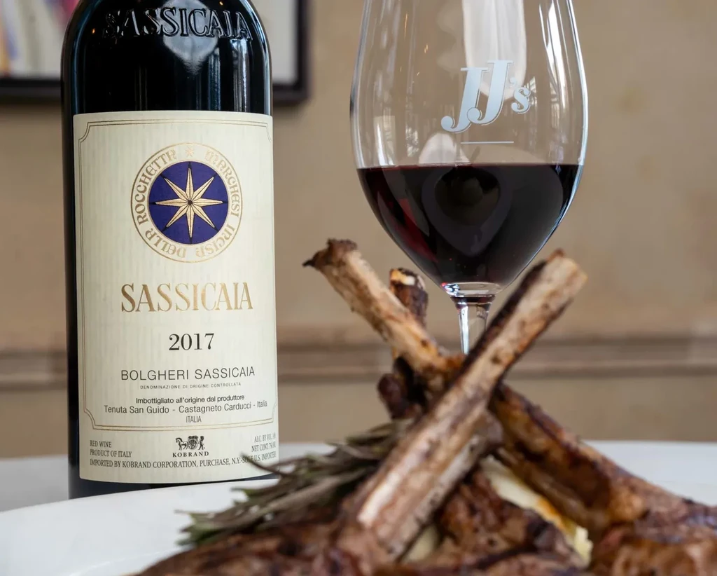 Sassicaia 2017 wine bottle, red wine, and lamb chops with rosemary.