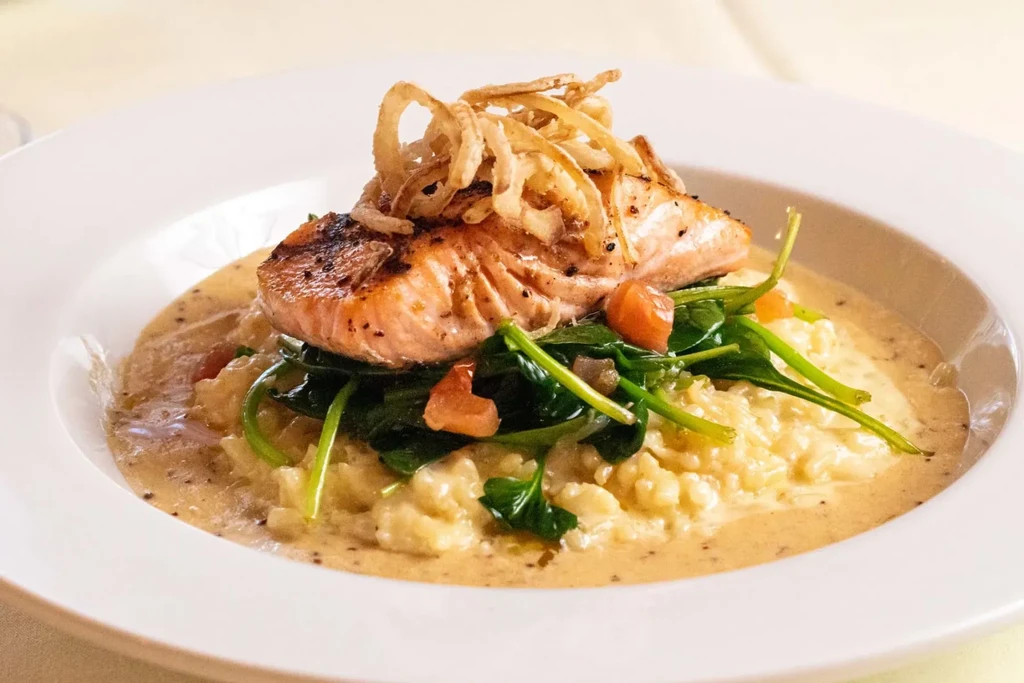 Pan-seared salmon, crispy fried onions, creamy risotto, spinach, and tomatoes.
