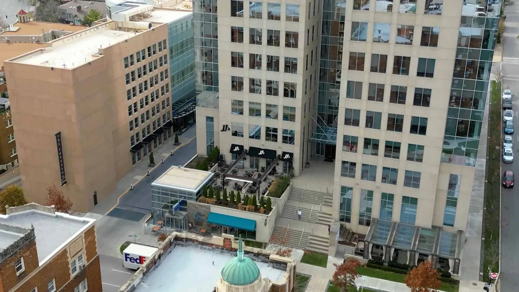 High-angle modern urban street with commercial buildings, outdoor seating, autumn trees.