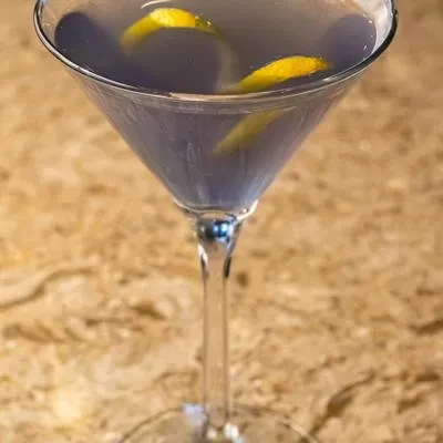 Martini glass with a lavender cocktail and two yellow lemon twists.