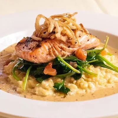 Pan-seared salmon with crispy onions, risotto, spinach, and creamy sauce.