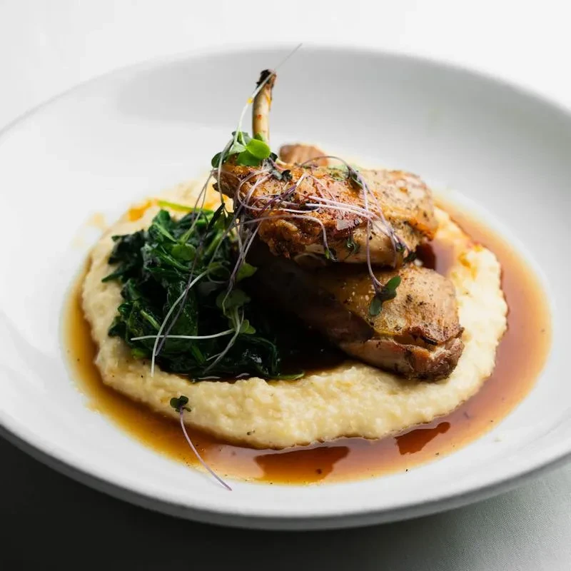 Plated dish: roasted meat, polenta, greens, brown sauce, microgreens.