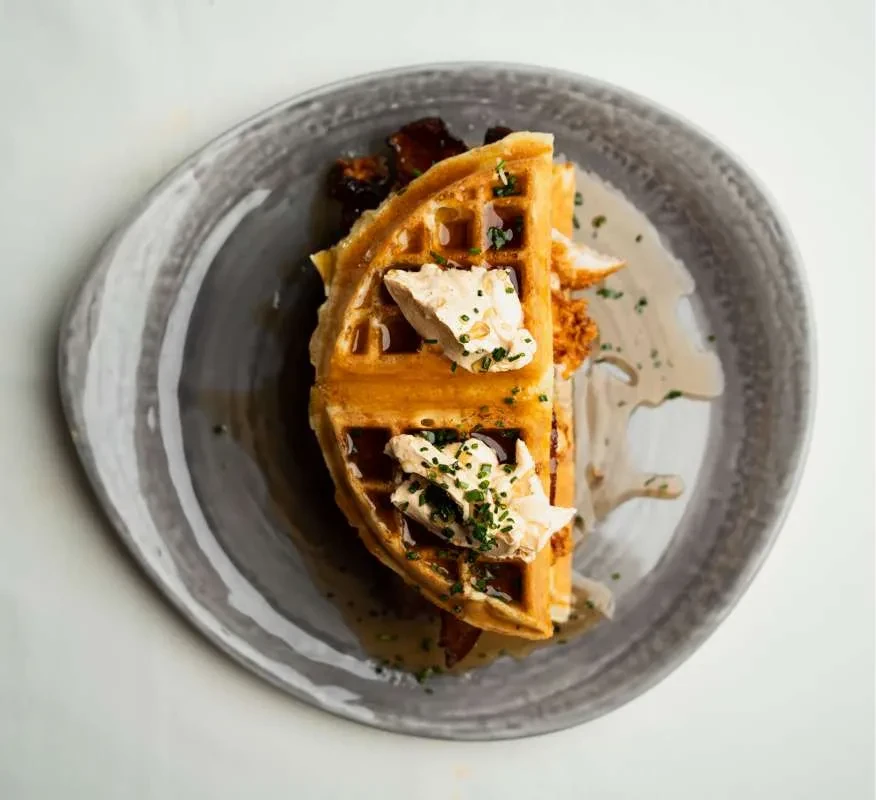 Savory waffle, fried chicken, creamy topping, and green herbs.