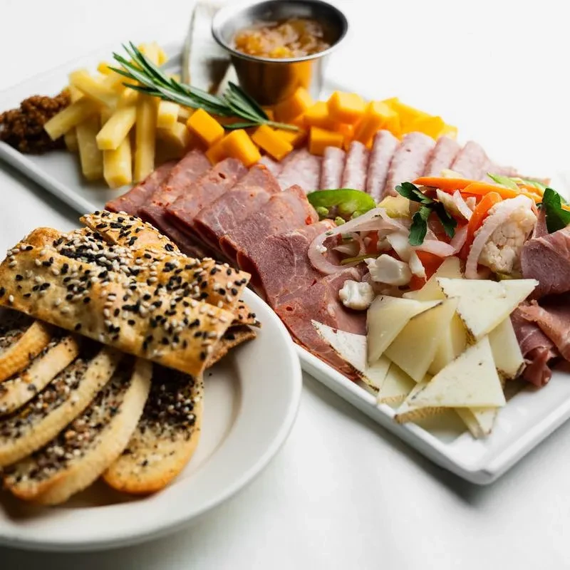 A generously portioned charcuterie board with meats, cheeses, crackers, pickles, and jam.