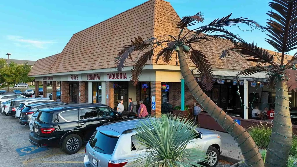 Exterior of Rudy's Taqueria with parking lot, people, and decorative palm trees.