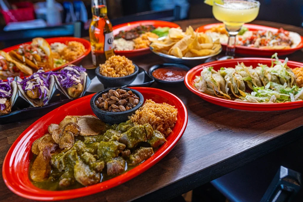 Colorful Mexican food, beer, and margarita on a wooden restaurant table.