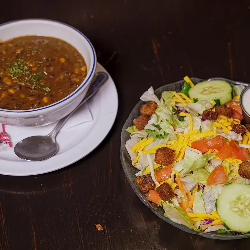 Dark soup with green herbs and a salad with cheese, tomatoes, cucumbers.