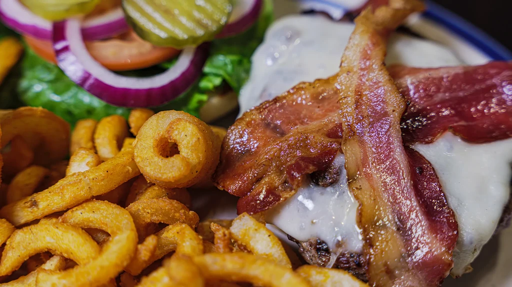 Close-up of a cheeseburger with bacon, curly fries, and salad.