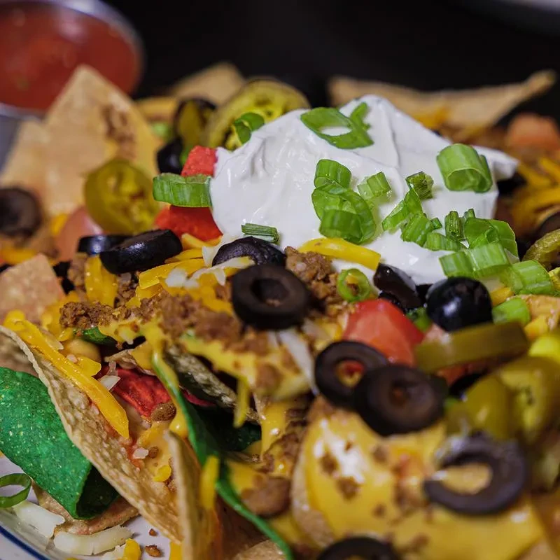 Close-up: Loaded nachos with cheese, meat, jalapeños, olives, sour cream.