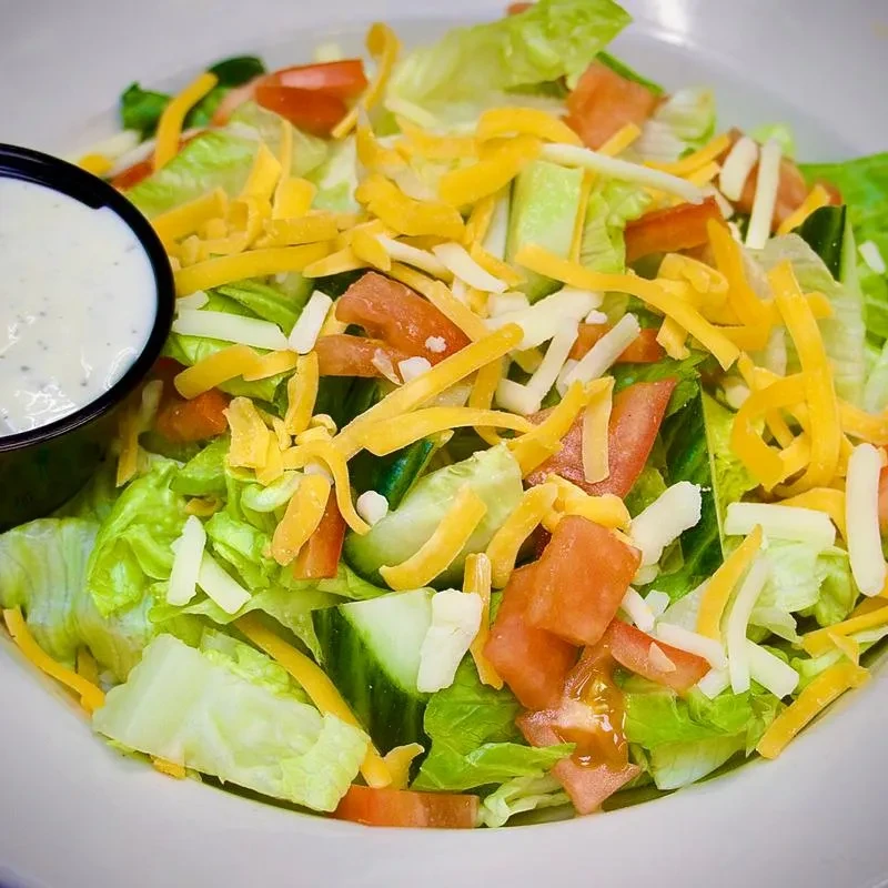 Fresh salad with lettuce, tomatoes, cucumber, cheese, and dressing.
