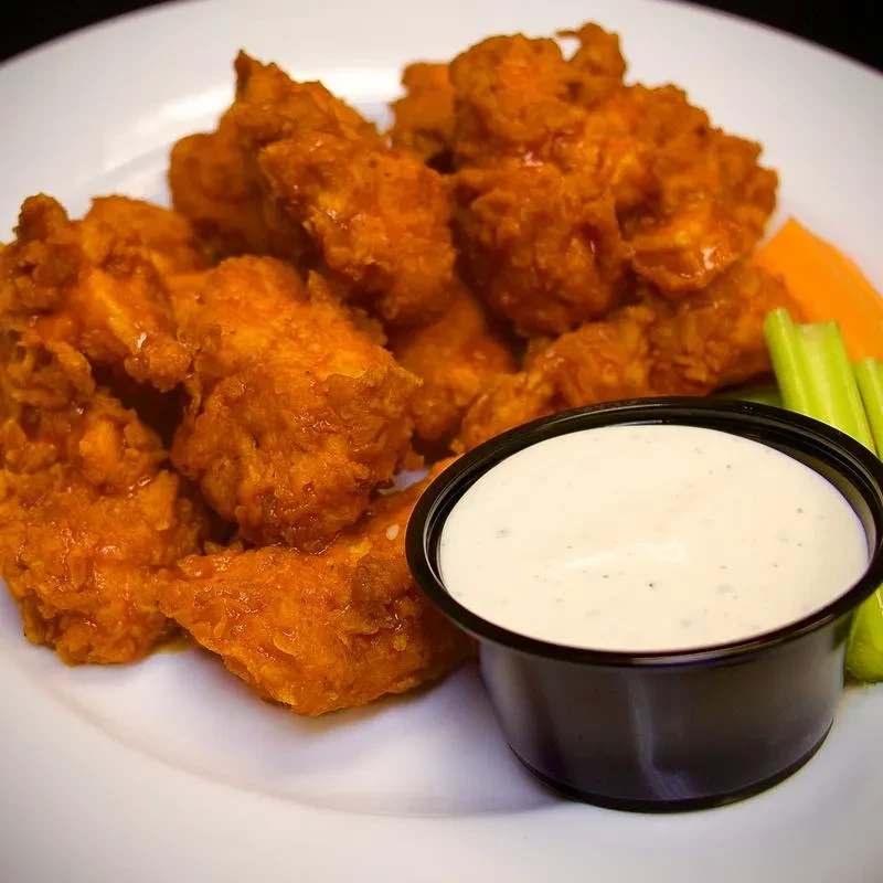 Boneless buffalo chicken bites with white dipping sauce, celery, and carrots.