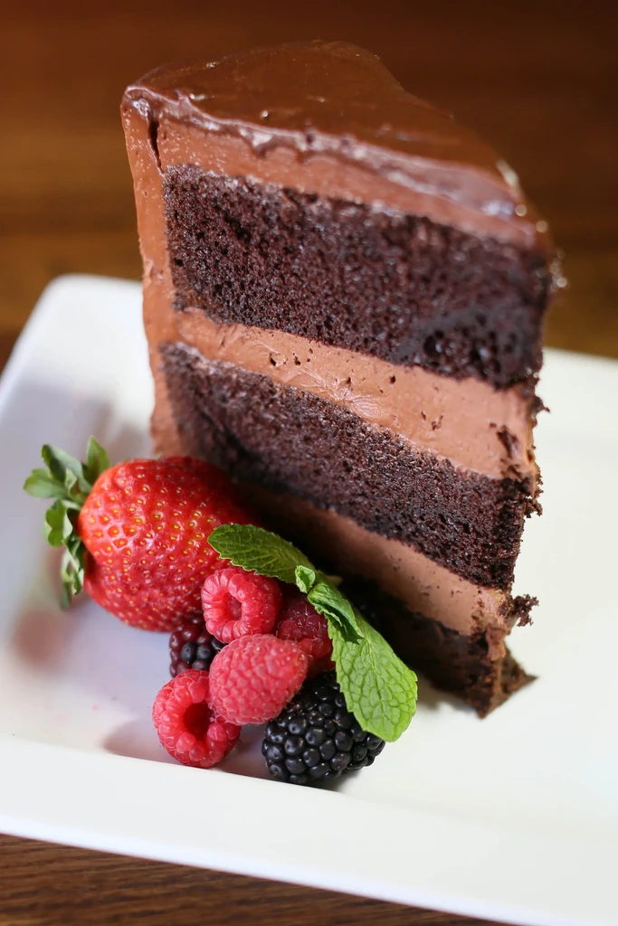 Close-up layered chocolate cake slice with ganache, berries, and mint.