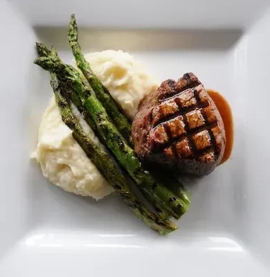 Plated grilled steak, mashed potatoes, and grilled asparagus with sauce.