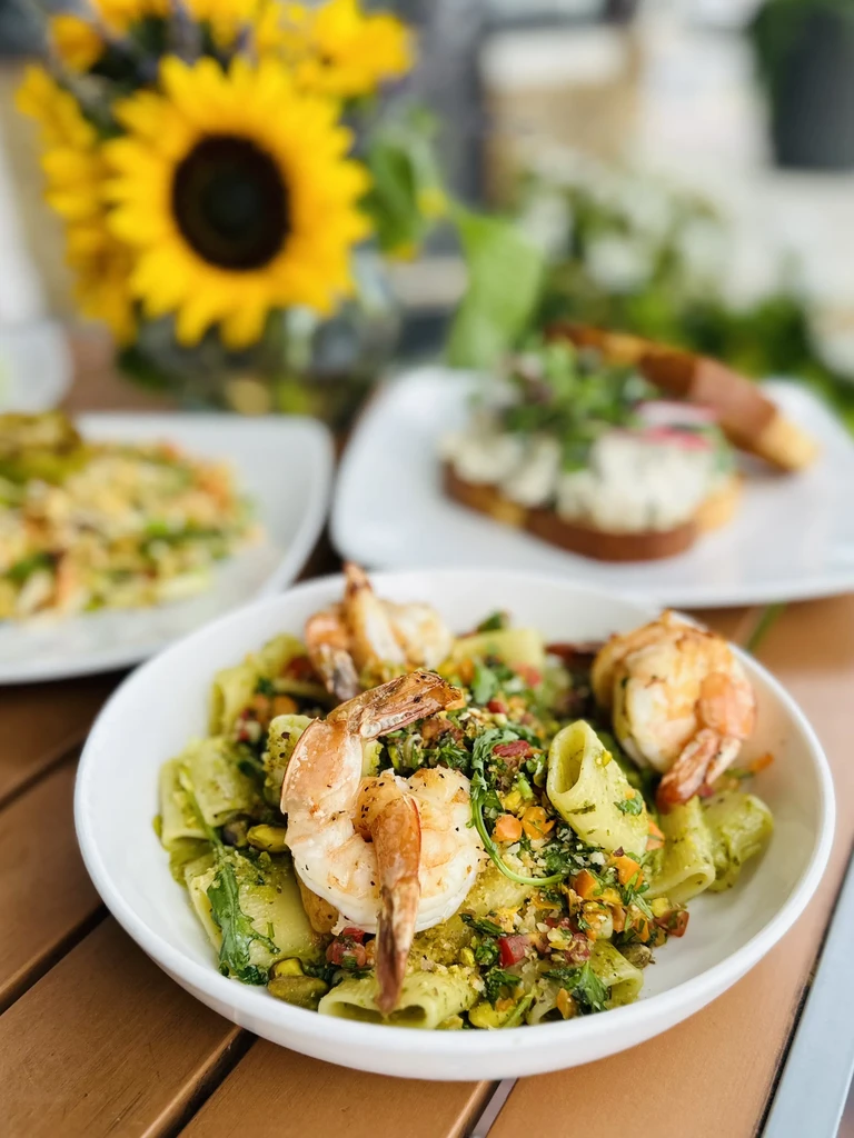 Close-up of rigatoni pasta with grilled shrimp, green sauce, vegetables, pistachios.