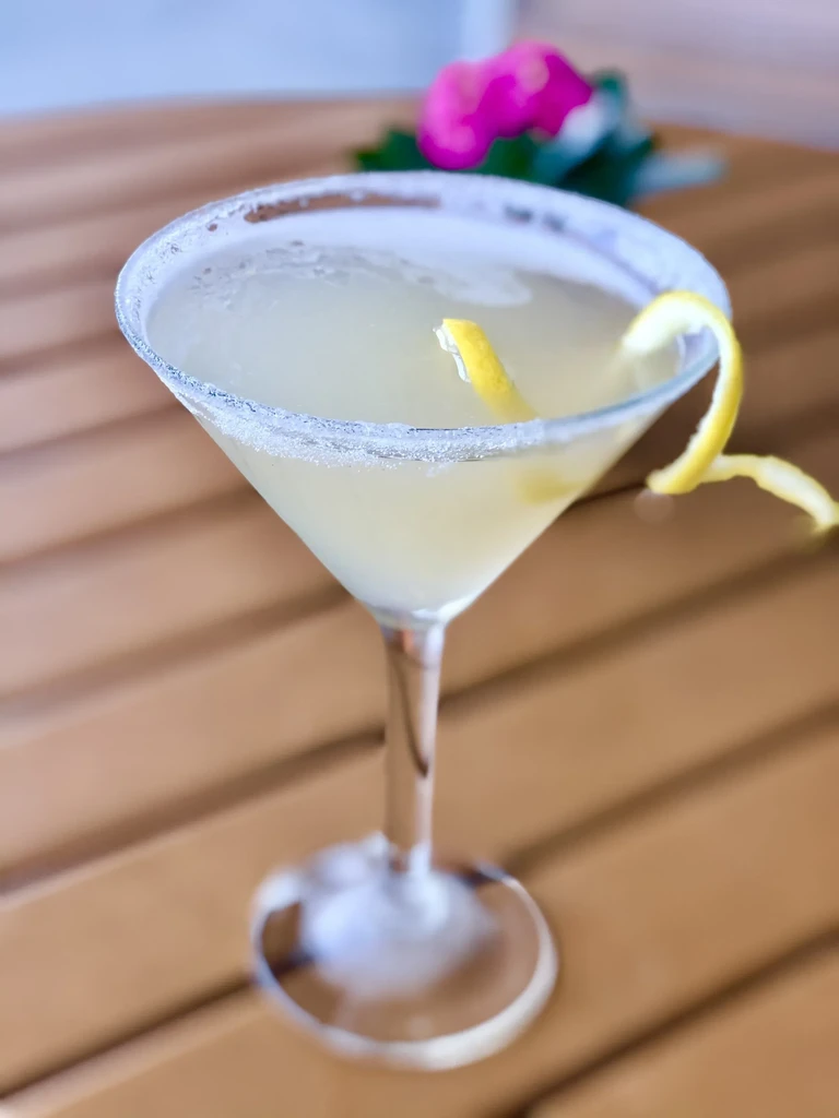 Frothy yellow cocktail in martini glass with sugared rim and lemon twist.