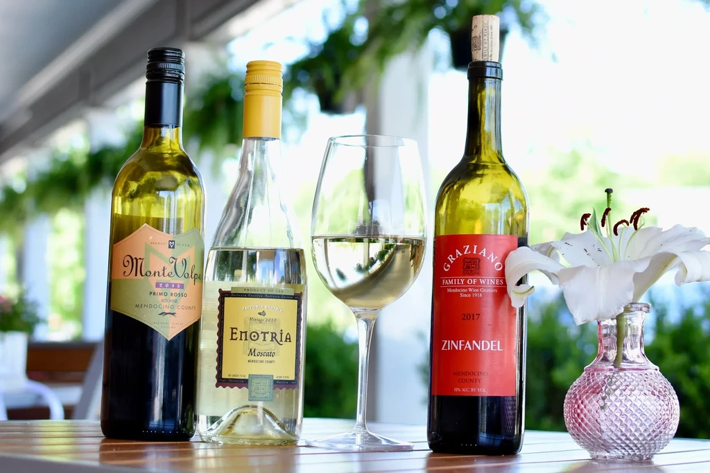 Wine bottles, glass of white wine, and lily vase outdoors.
