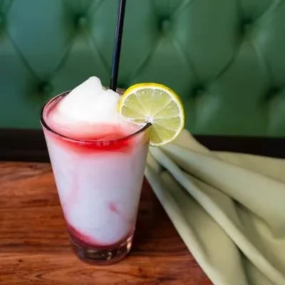 Layered frozen drink with lime and straw on a wooden table.