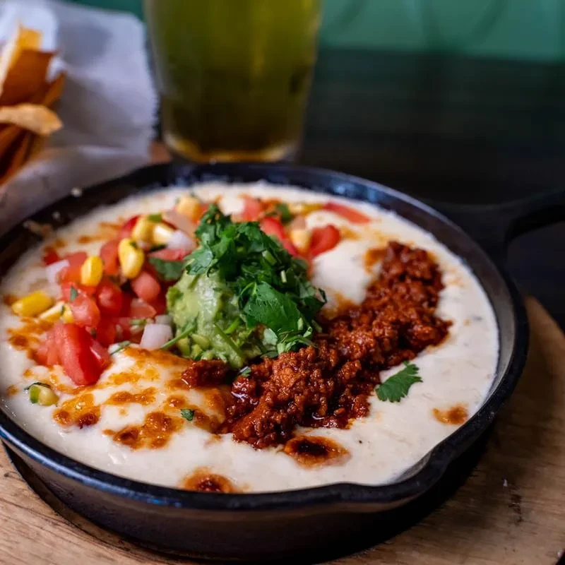 Skillet of queso fundido topped with pico, corn, guacamole, and chorizo.