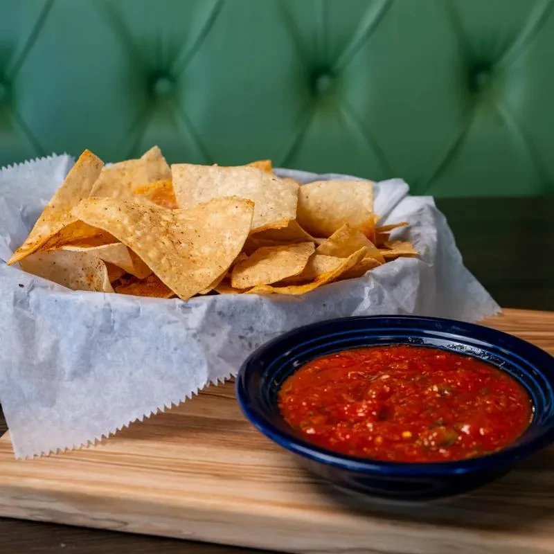 Basket of tortilla chips and chunky red salsa in a restaurant.