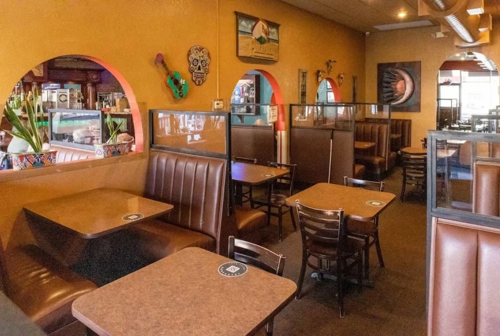 Empty restaurant interior with booths, orange walls, colorful decor, and bar.