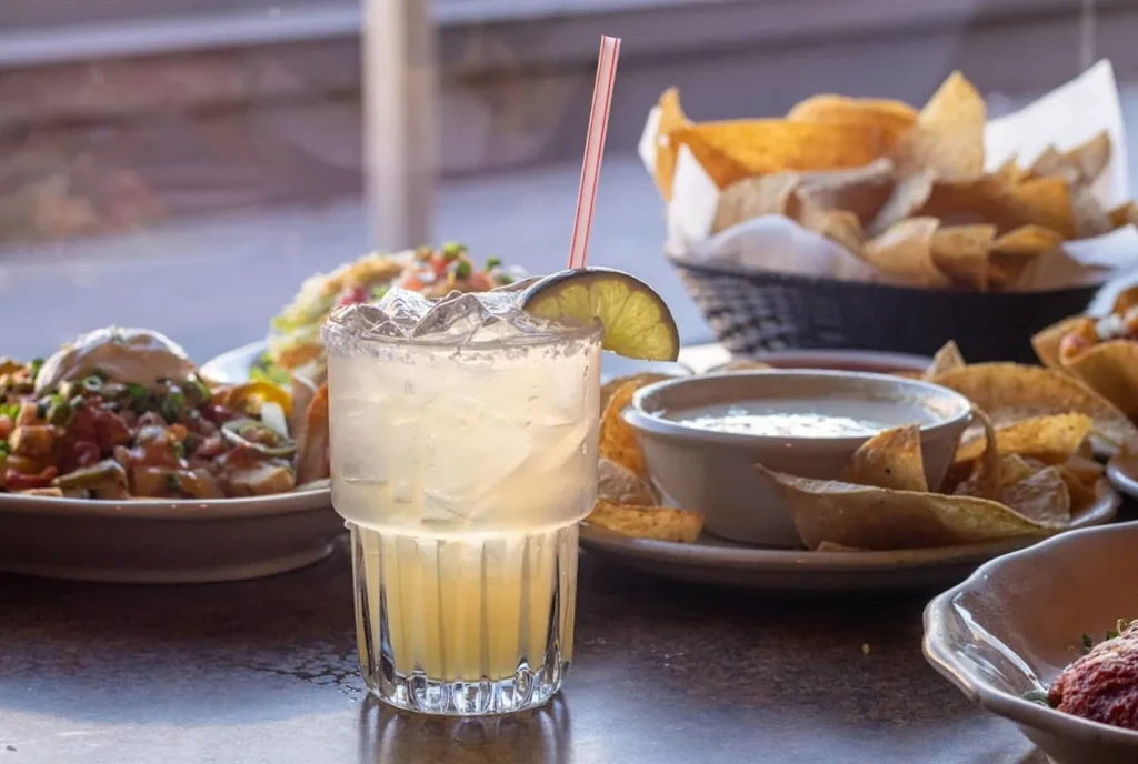 Iced margarita, nachos, queso dip, and tortilla chips on a table.