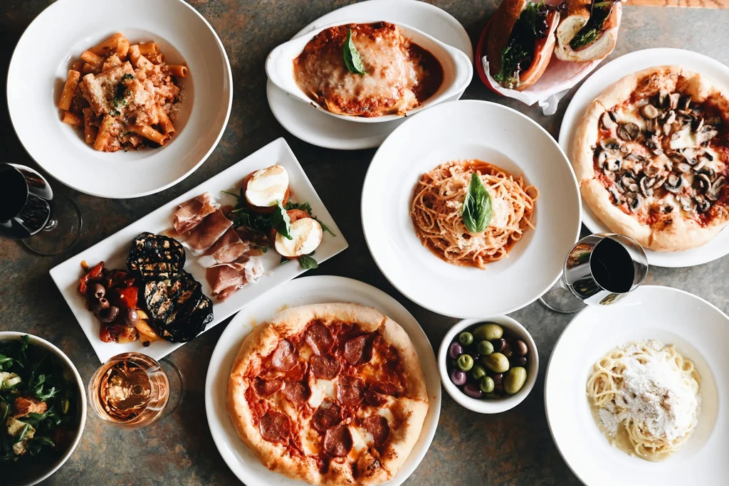 Flat-lay photo of various Italian pizzas, pastas, antipasto, and wines.