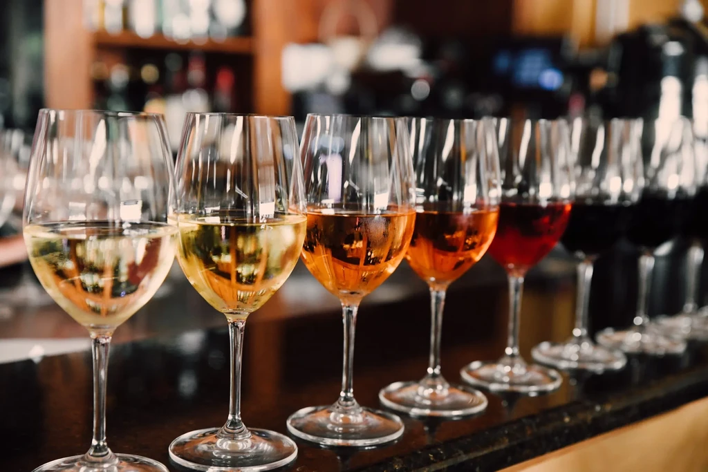 A row of wine glasses filled with various colored wines on a bar.