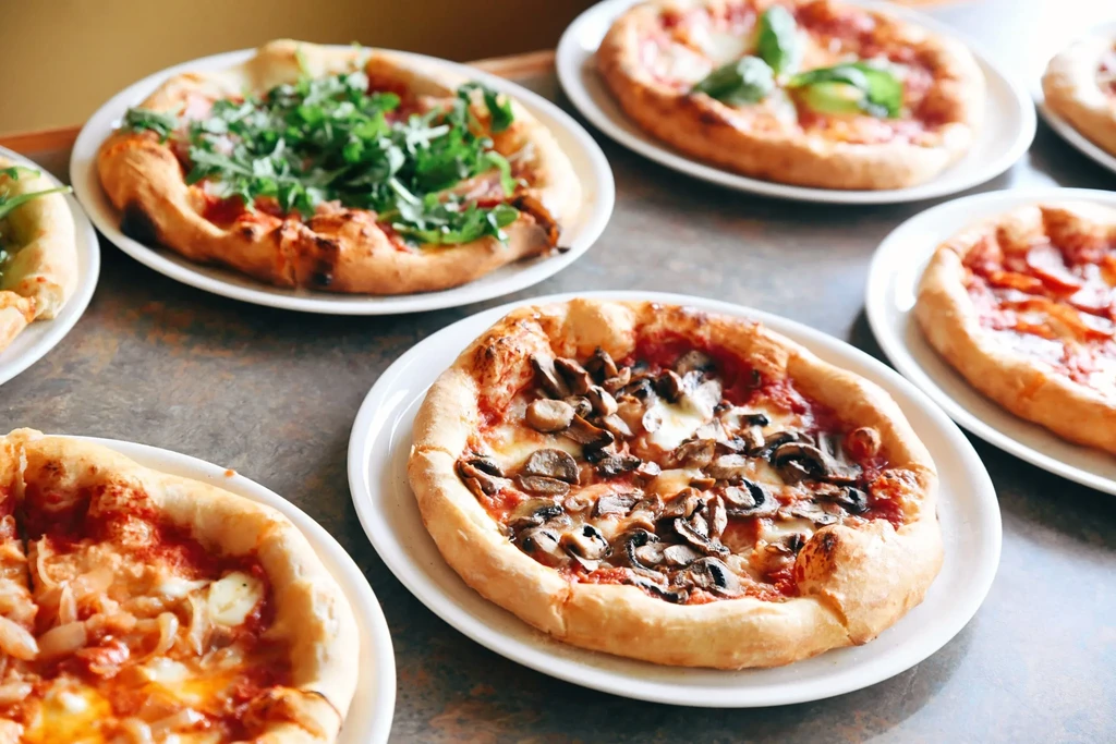 Six individual pizzas, including mushroom and arugula, on a dark table.