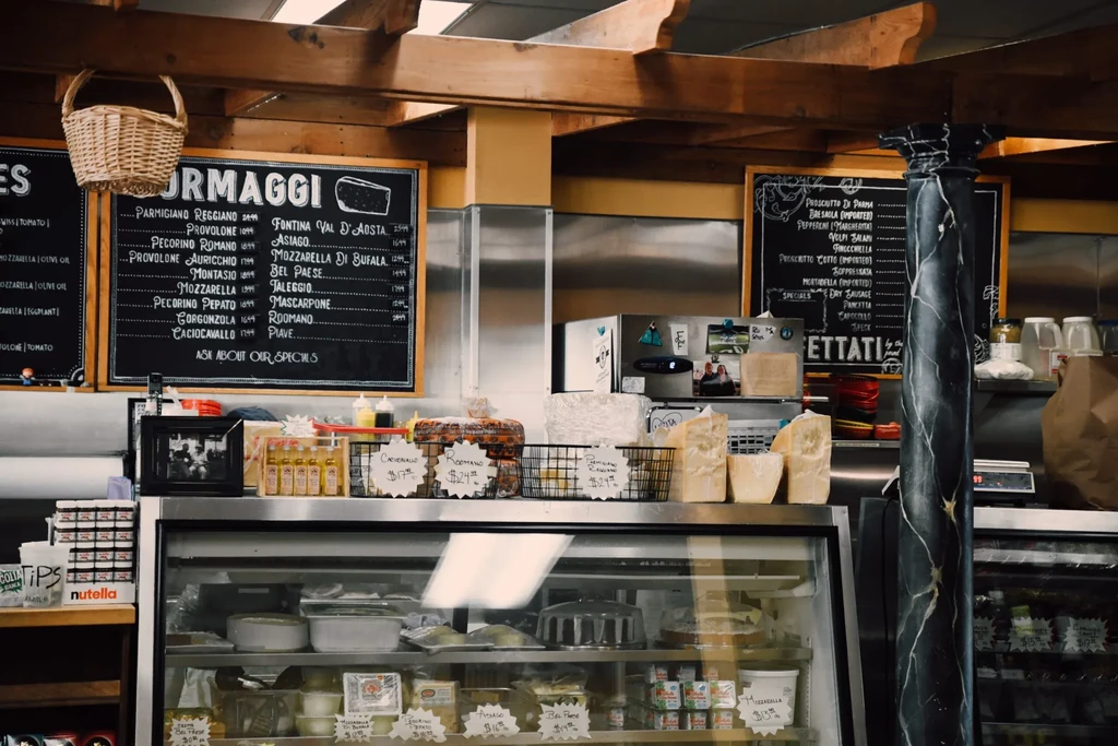 Refrigerated deli display of cheeses and specialty foods with chalkboards.