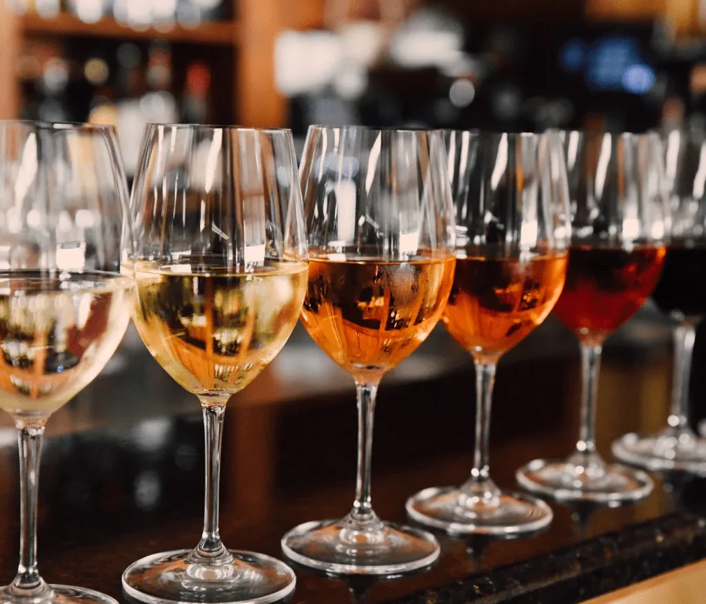 Wine glasses in a row, filled with white, amber, and red wines.