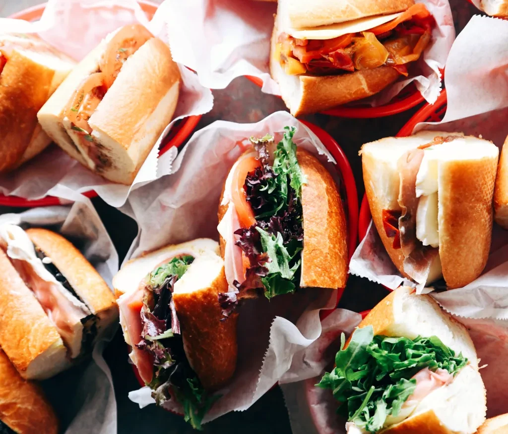 Eight deli-style sandwiches with diverse fresh fillings, some in baskets.