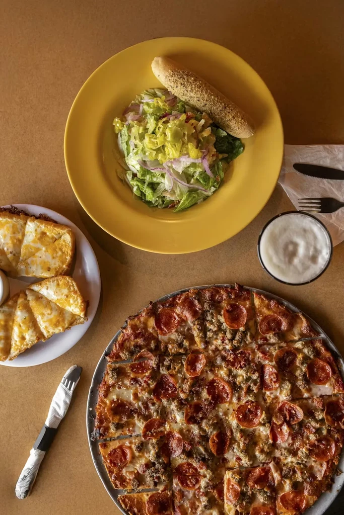 Overhead food spread: pepperoni pizza, green salad, cheesy bread.