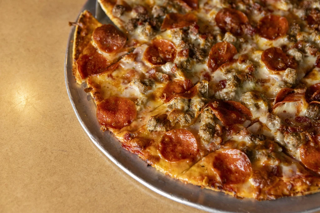 Freshly baked pepperoni and sausage pizza on pan, one slice removed.