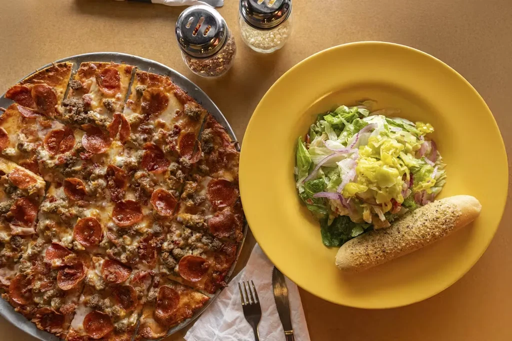 High-angle view of pepperoni pizza, green salad, breadstick, and condiments.