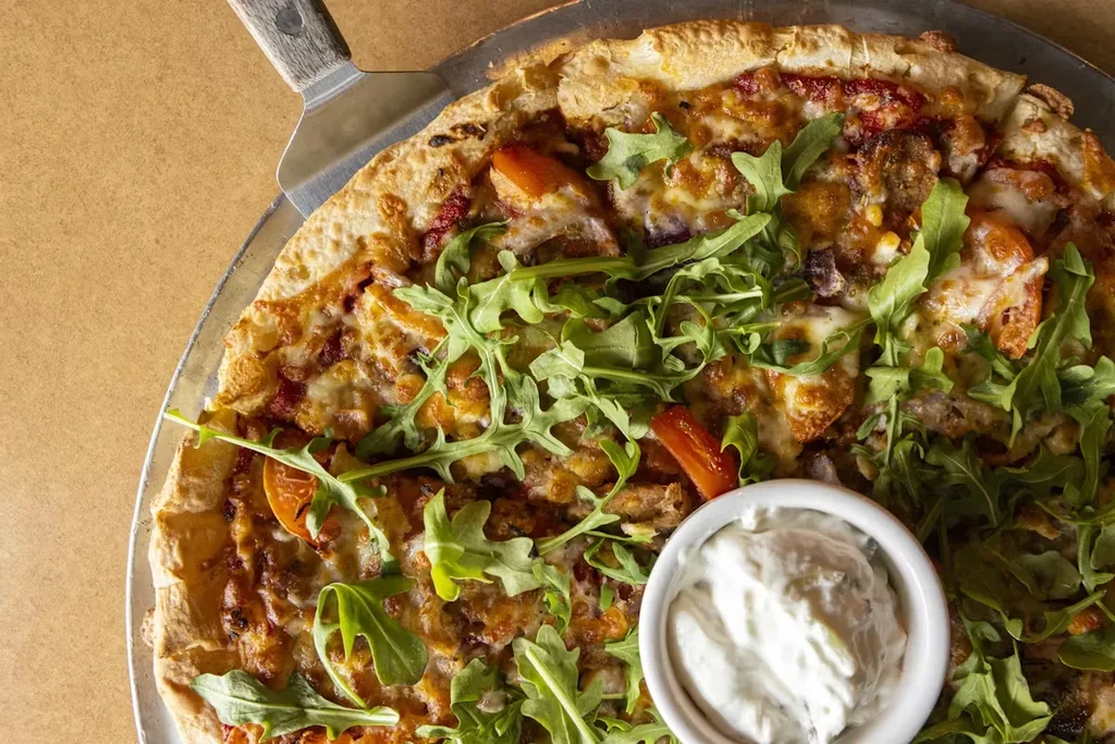Freshly baked pizza with arugula, meat, cheese, and dipping sauce.