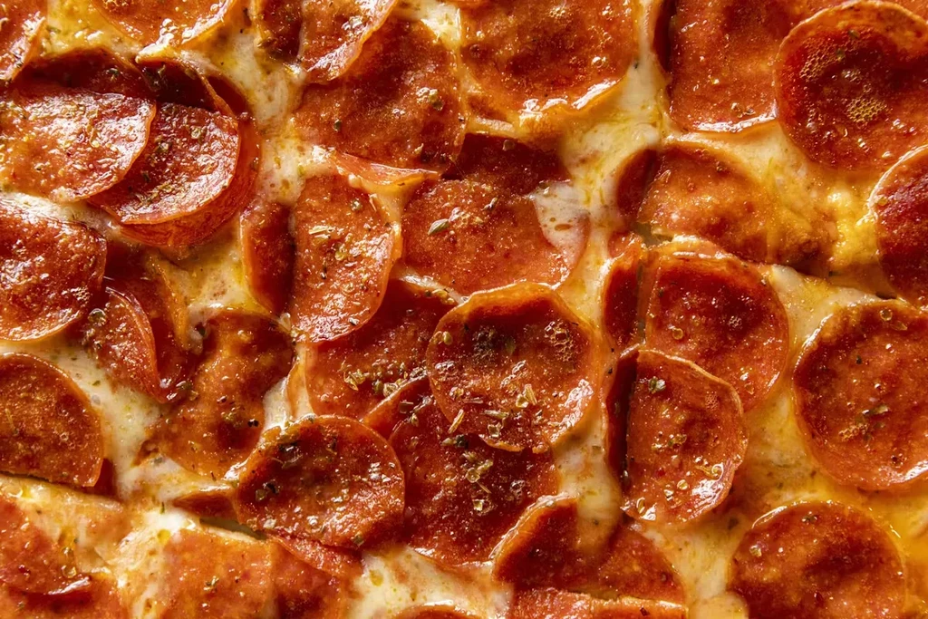 Close-up of hot pepperoni pizza with bubbly cheese and green herbs.