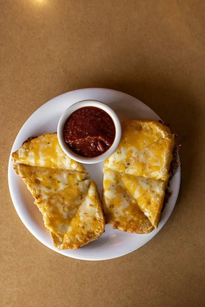 Plate of golden brown cheesy bread triangles with herbs and marinara.