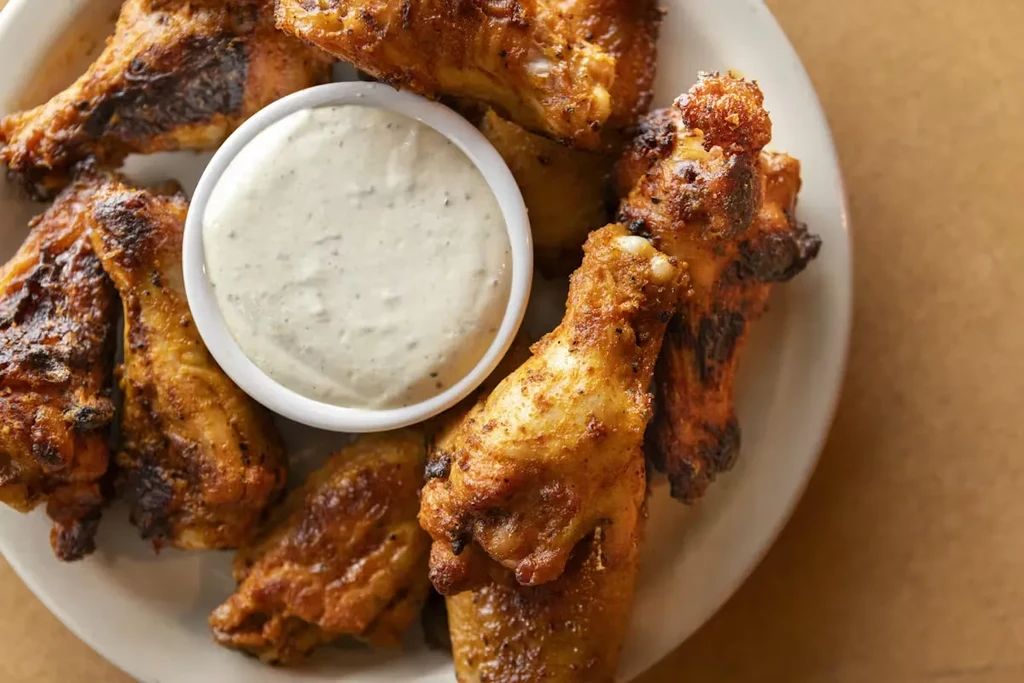 Crispy golden-brown chicken wings with creamy herb dipping sauce on a white plate.