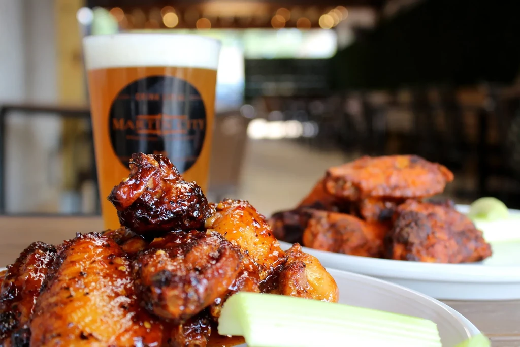 Two plates of glazed chicken wings with celery and a glass of beer.
