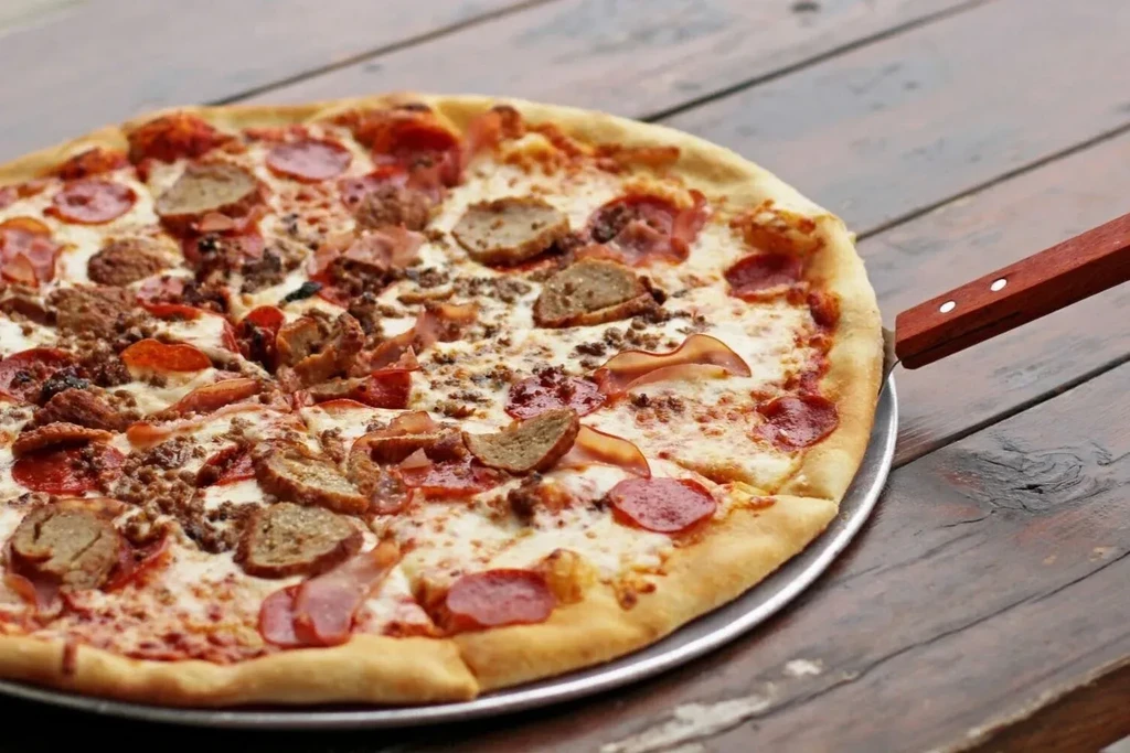 Round pizza with pepperoni, sausage, and cheese on a metal pan.