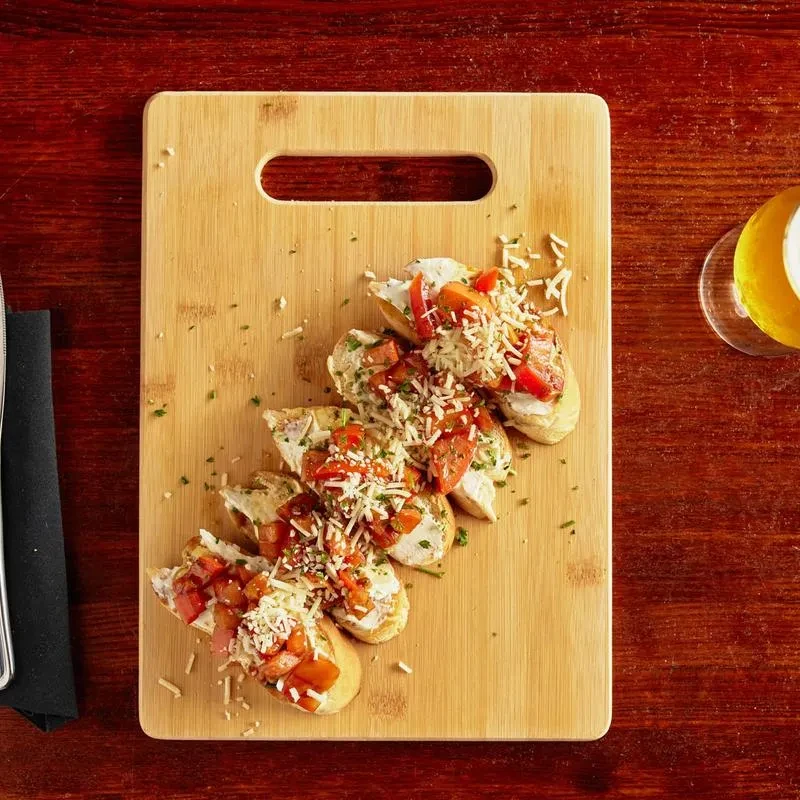 Six tomato, cheese, and herb crostini on a wooden serving board.